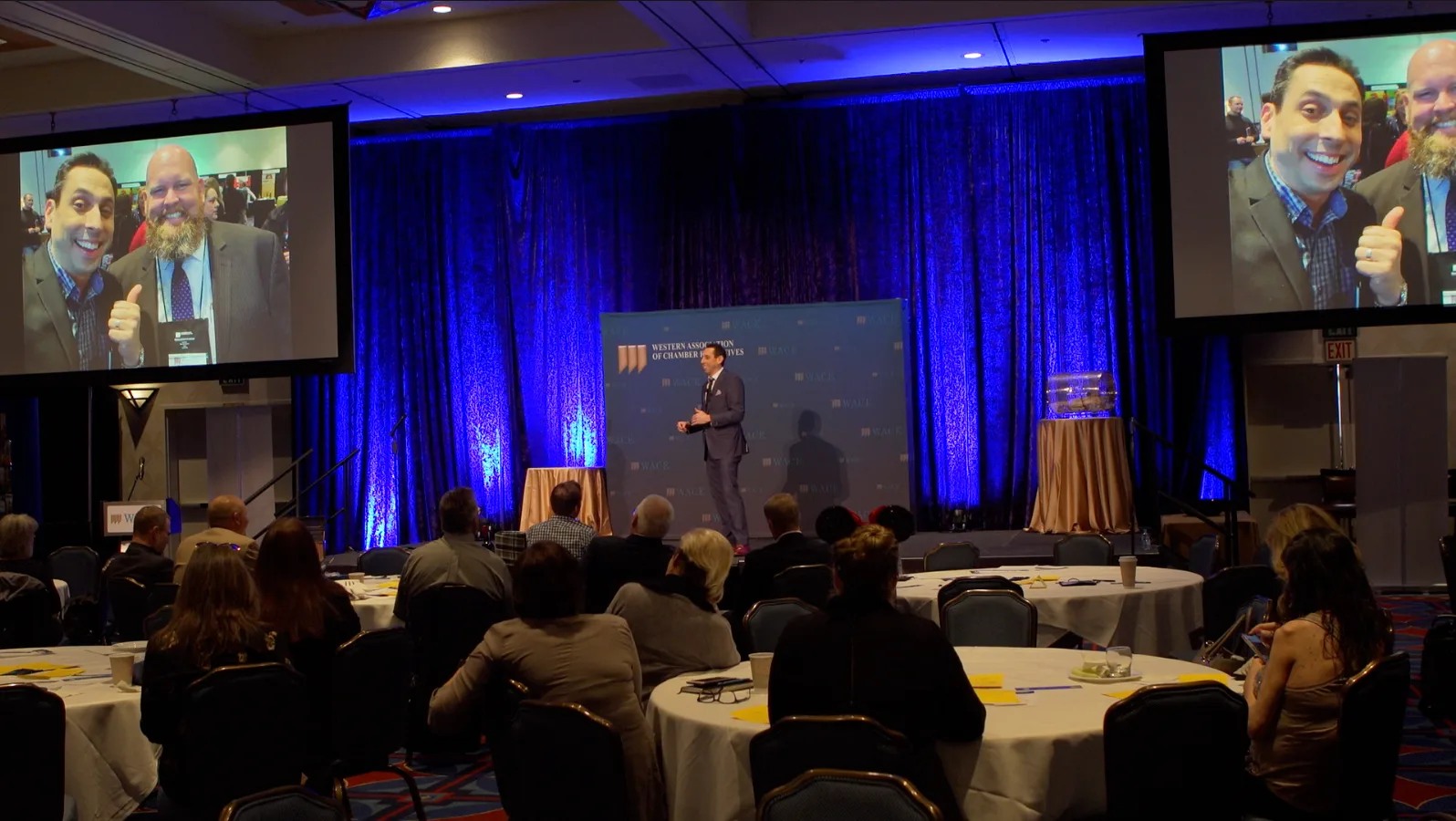 Jess Todtfeld speaking on stage under blue lighting at a live event