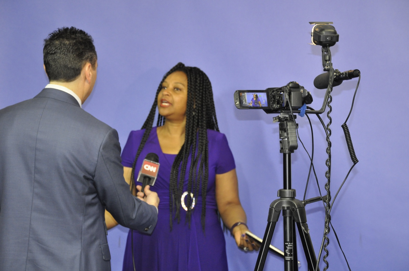 Man and woman conduct on-camera interview against blue backdrop studio.